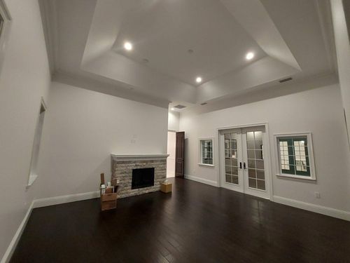 Empty living room with dark wood floors, white walls, tray ceiling, fireplace, and French doors.