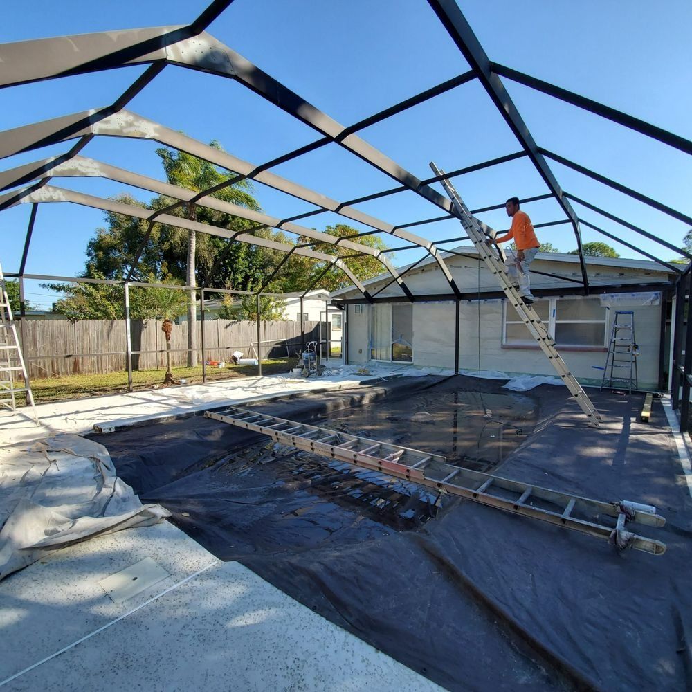Partially built backyard pool enclosure with worker on roof framing under blue sky