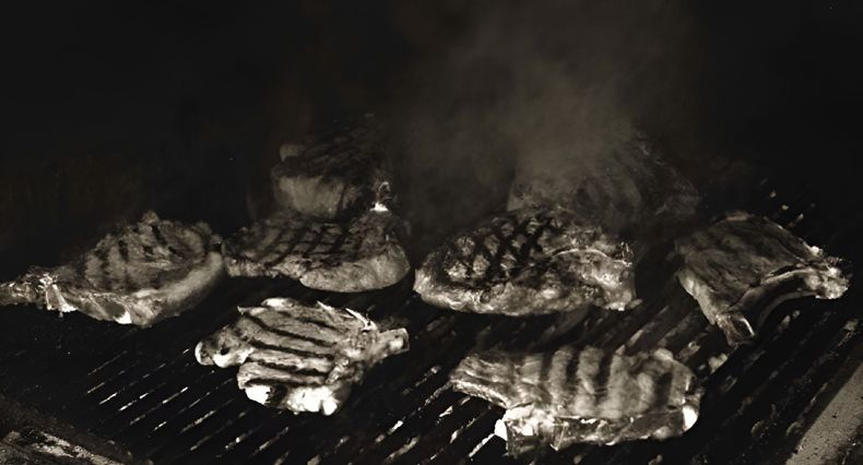 Bistecche grigliate su una griglia per barbecue affumicata, con segni di bruciatura ben visibili.