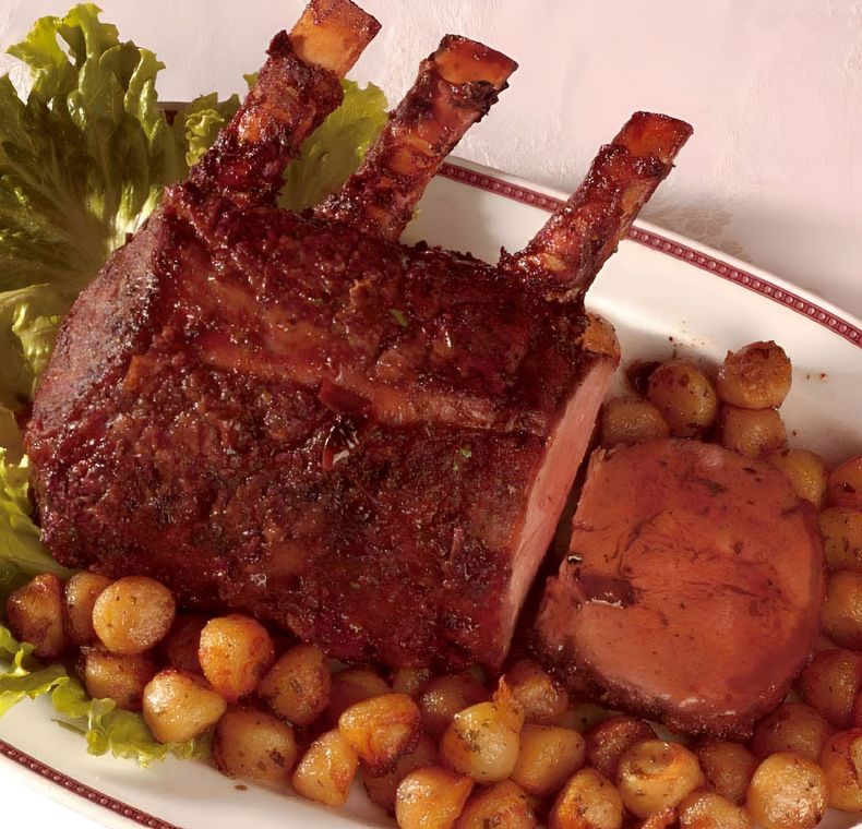 Costolette di maiale arrosto con crosta croccante, patate e verdure su un piatto bianco.