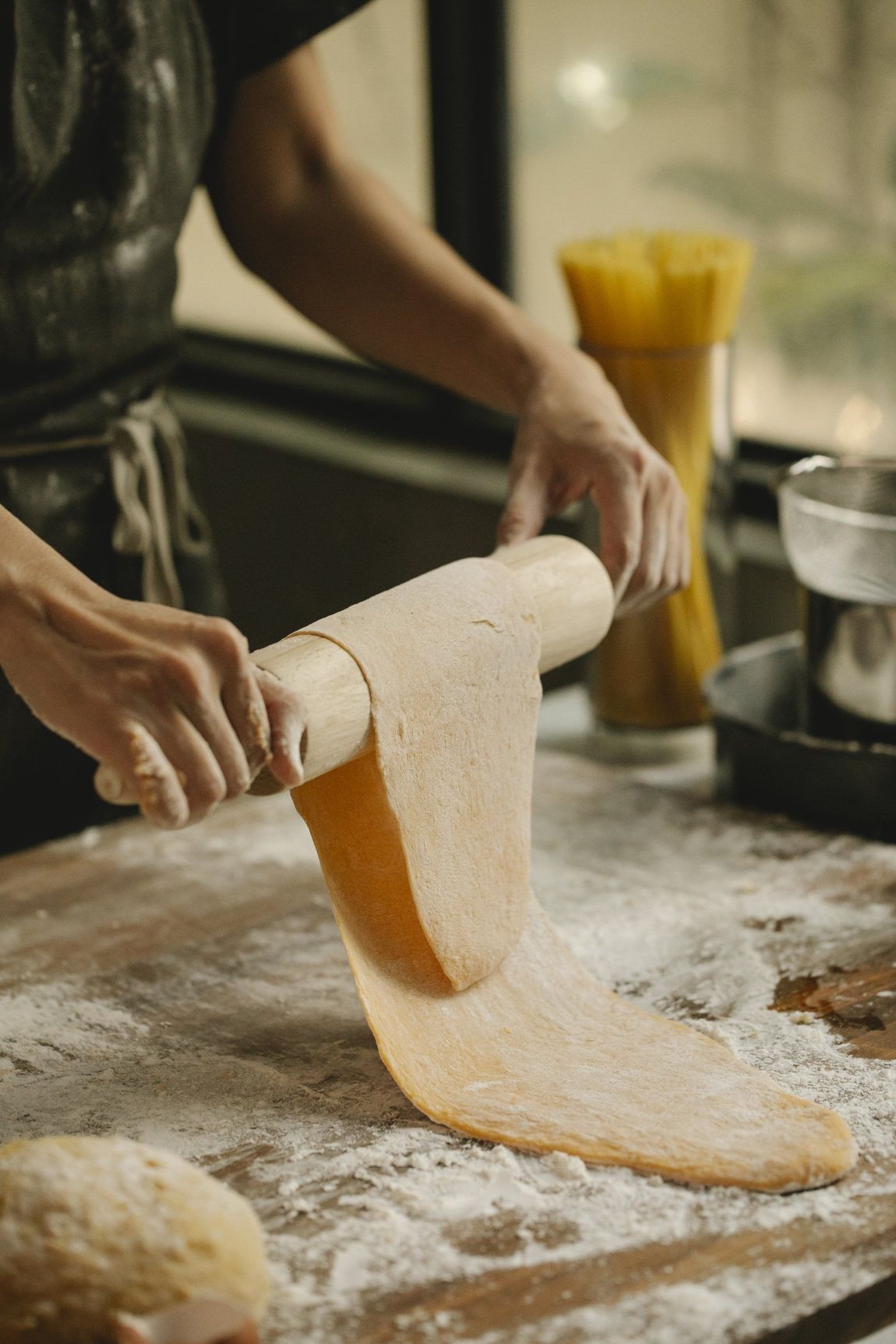 Mani che stendono la pasta fresca su un piano di lavoro infarinato in cucina.