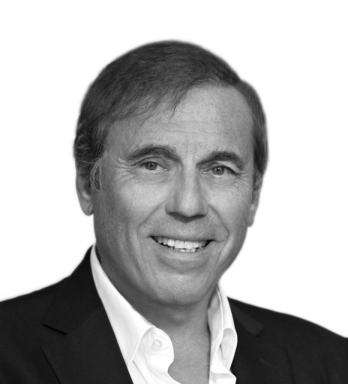 Un hombre con traje y camisa blanca sonríe en una foto en blanco y negro.