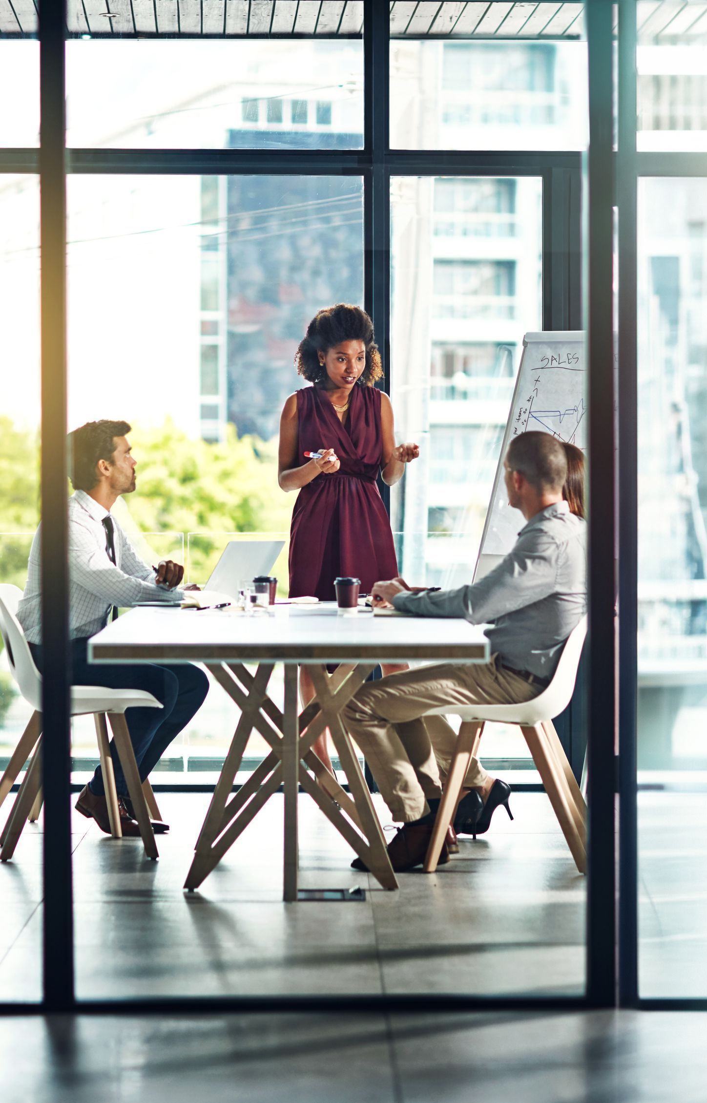 Business colleagues in a meeting, with a woman leading the presentation, near a whiteboard.