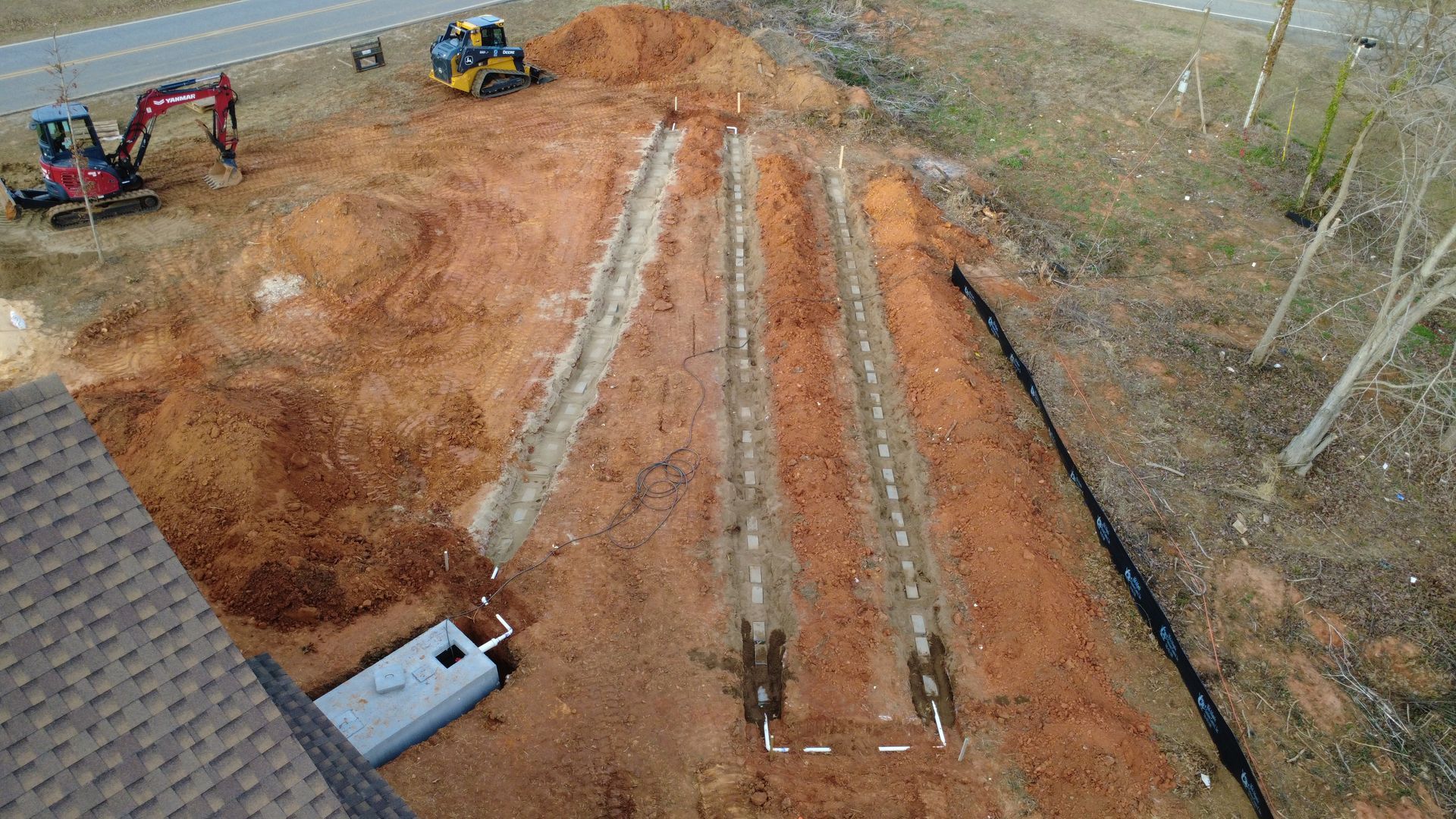 Aerial view of a dirt construction site with long graded strips and two excavators at the top left.
