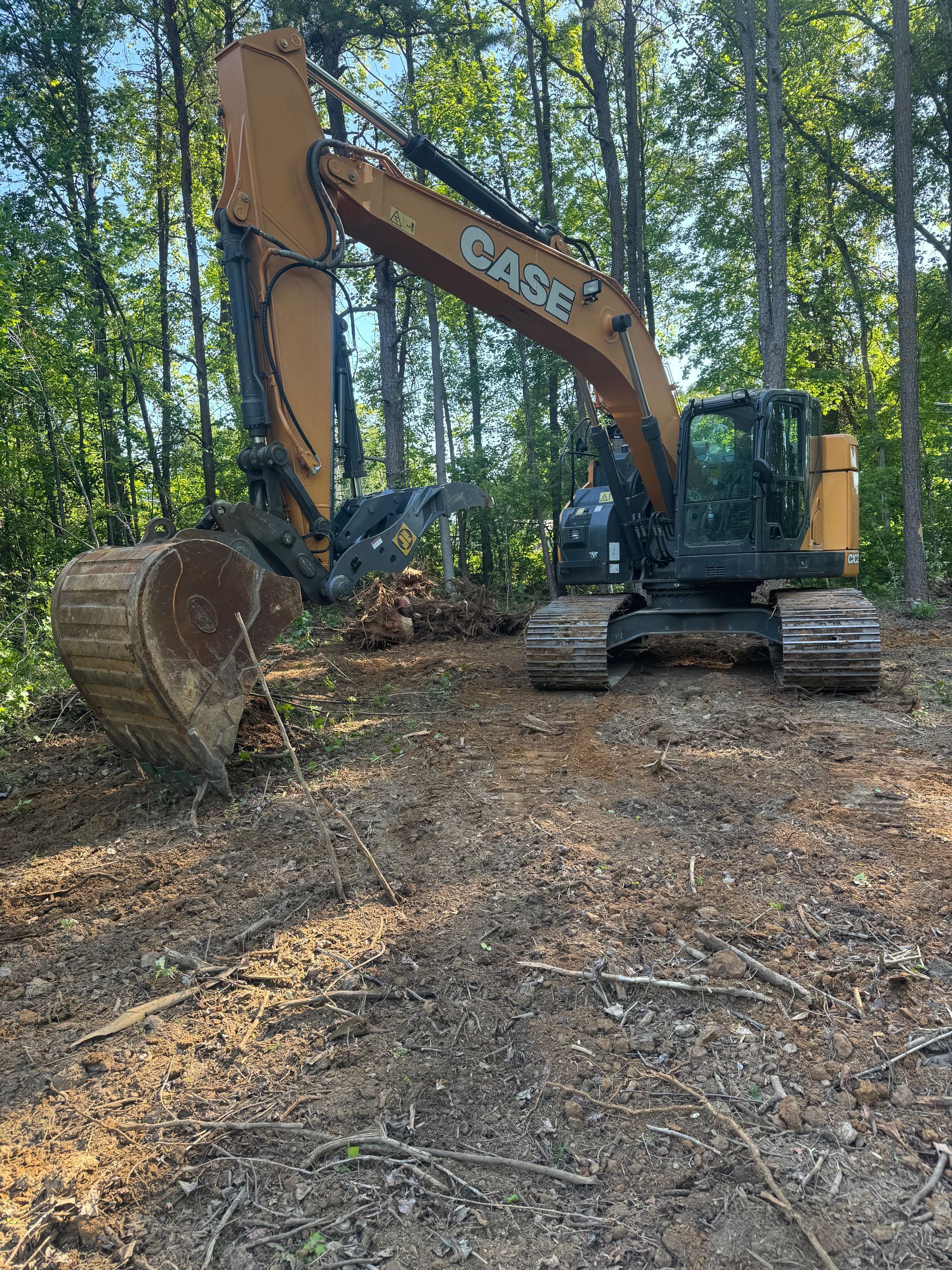 Excavator clearing a wooded area, with a large log bucket in a forest setting.