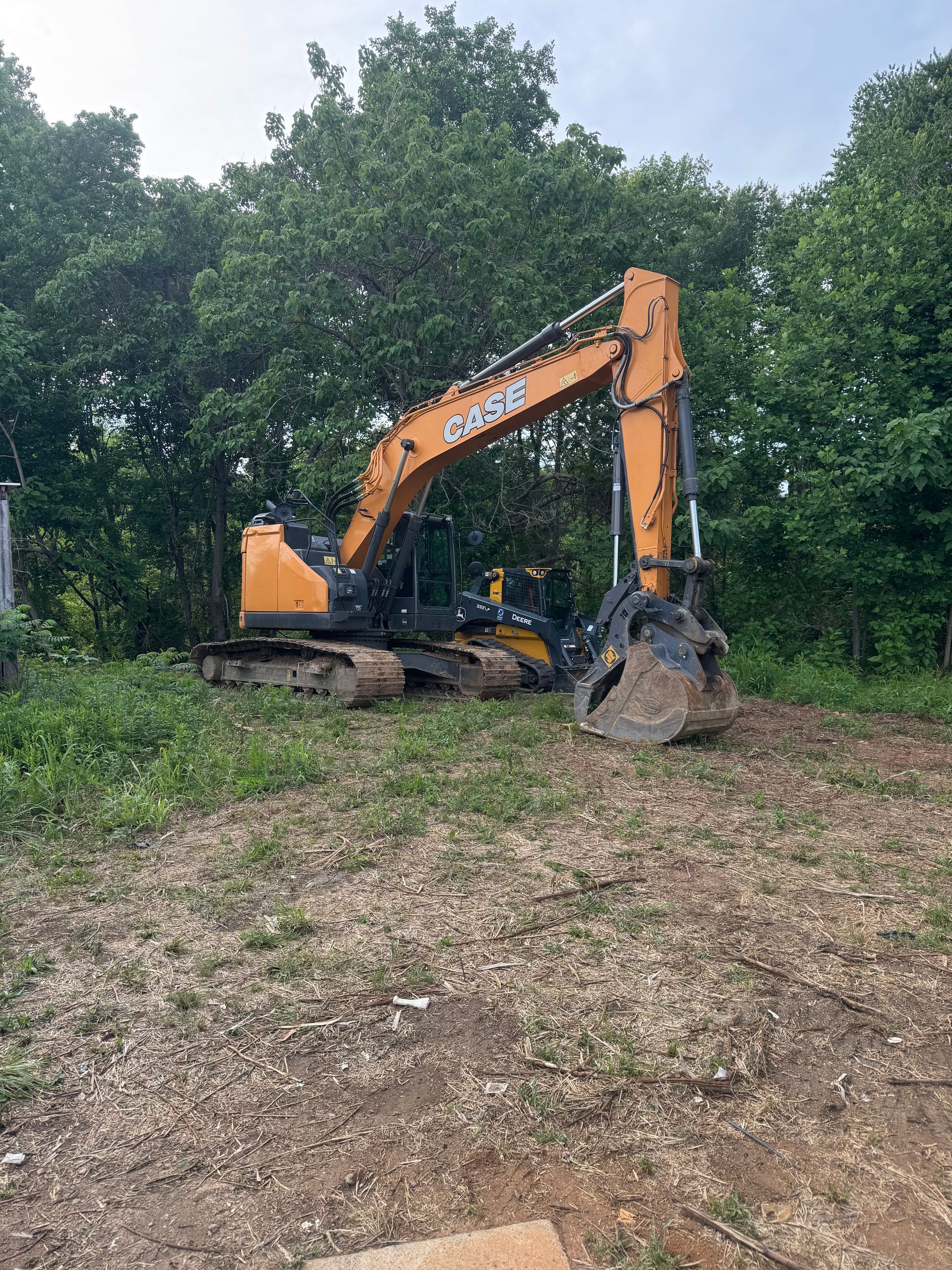 Orange excavator clearing ground near dense green trees
