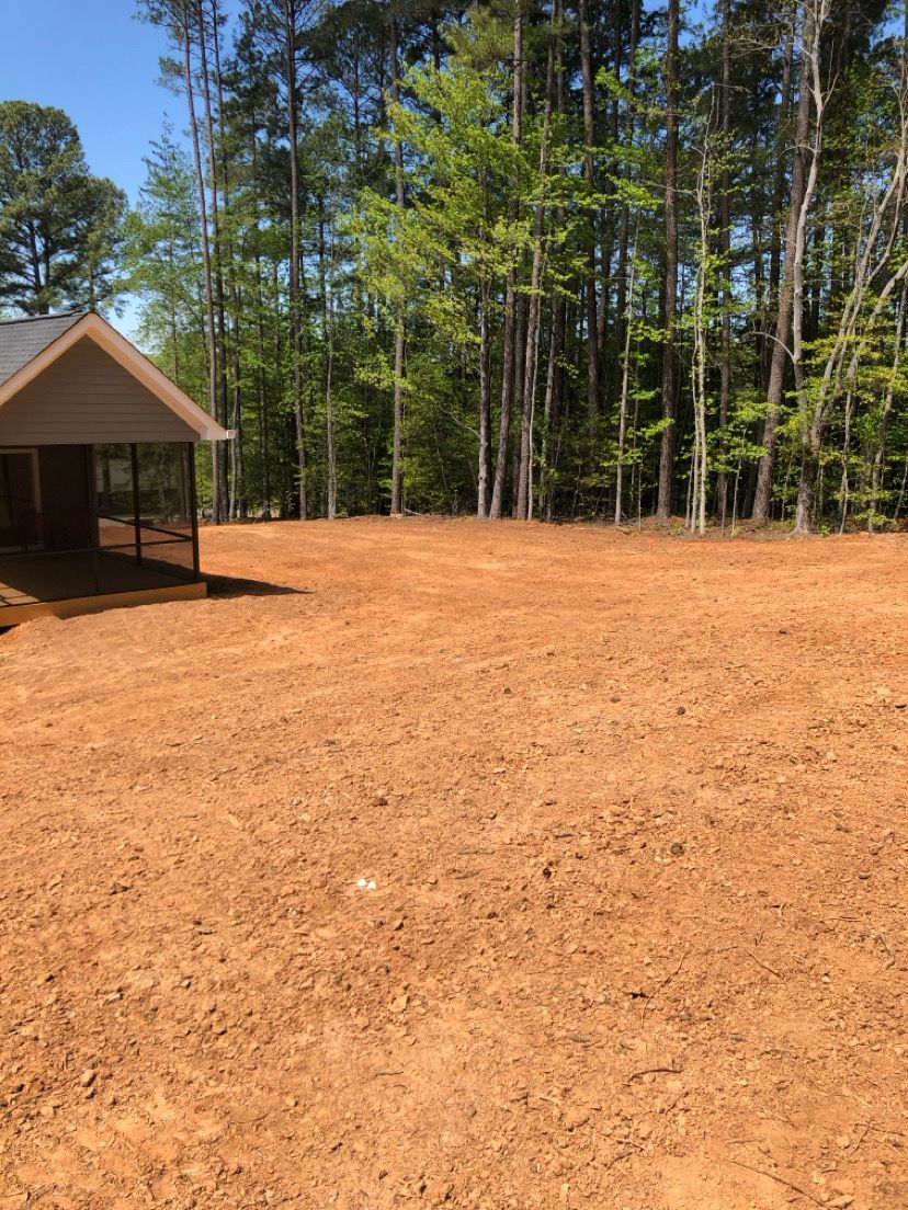 Small cabin beside a large cleared dirt area with tall trees in the background
