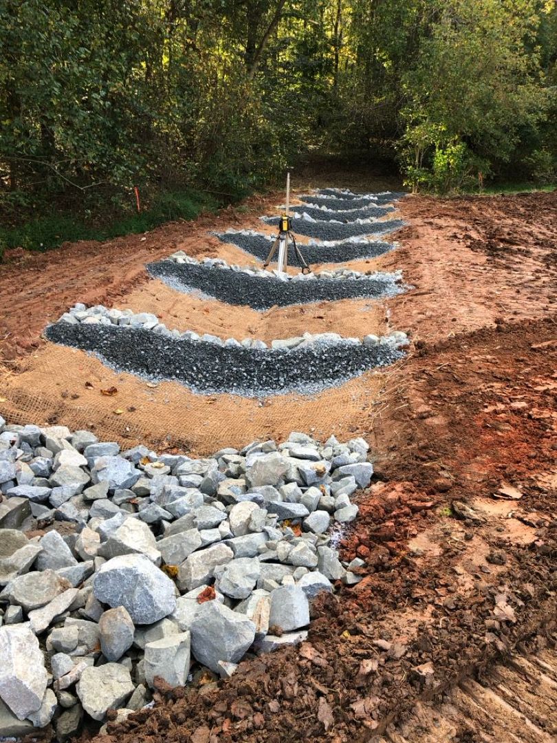 Rock-lined hillside steps under construction beside a dirt path in a wooded area