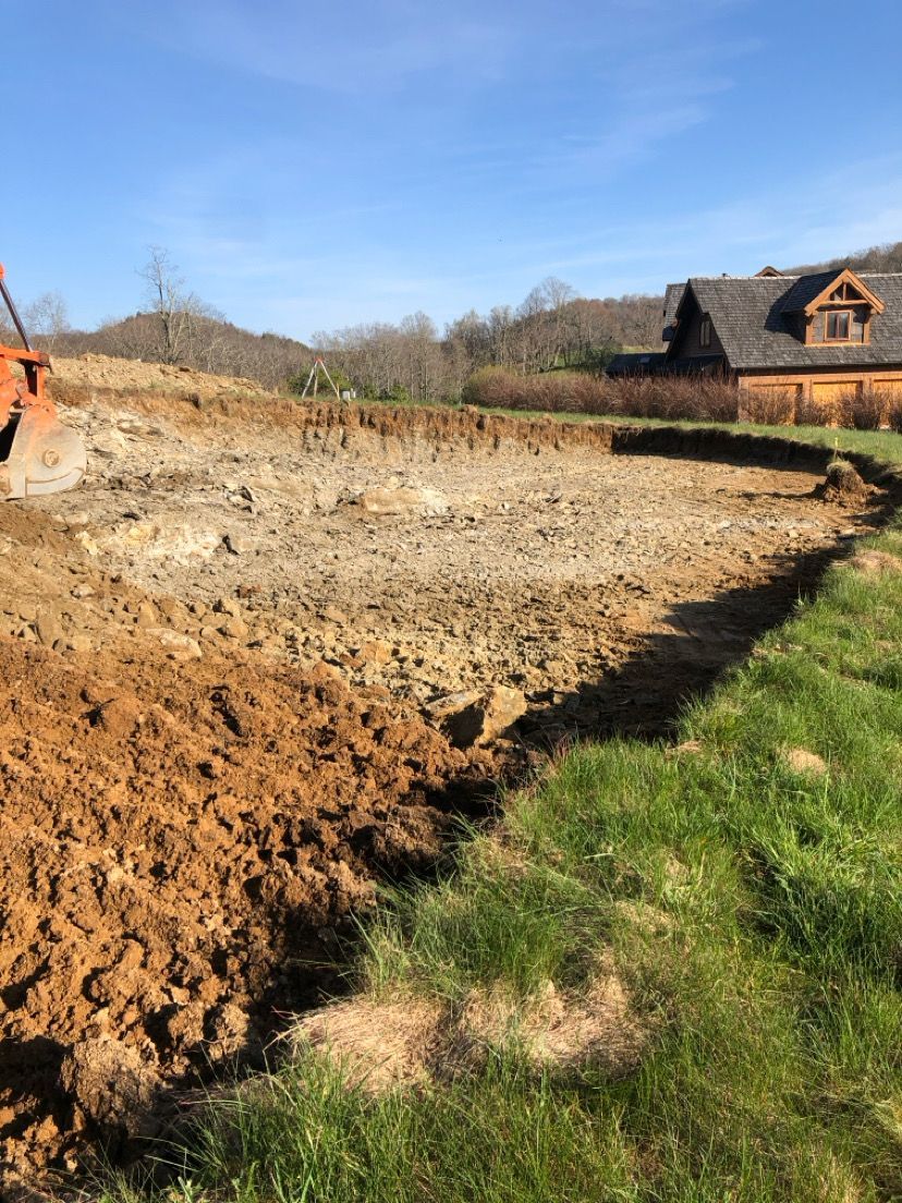 Cleared dirt lot under blue sky with houses in the background and a grassy edge in front