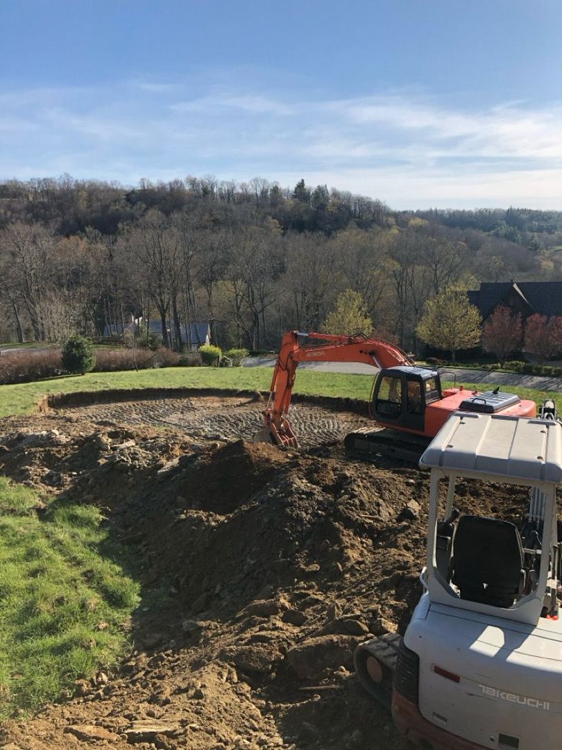 Excavator digging a large dirt pit beside a grassy field under a clear sky