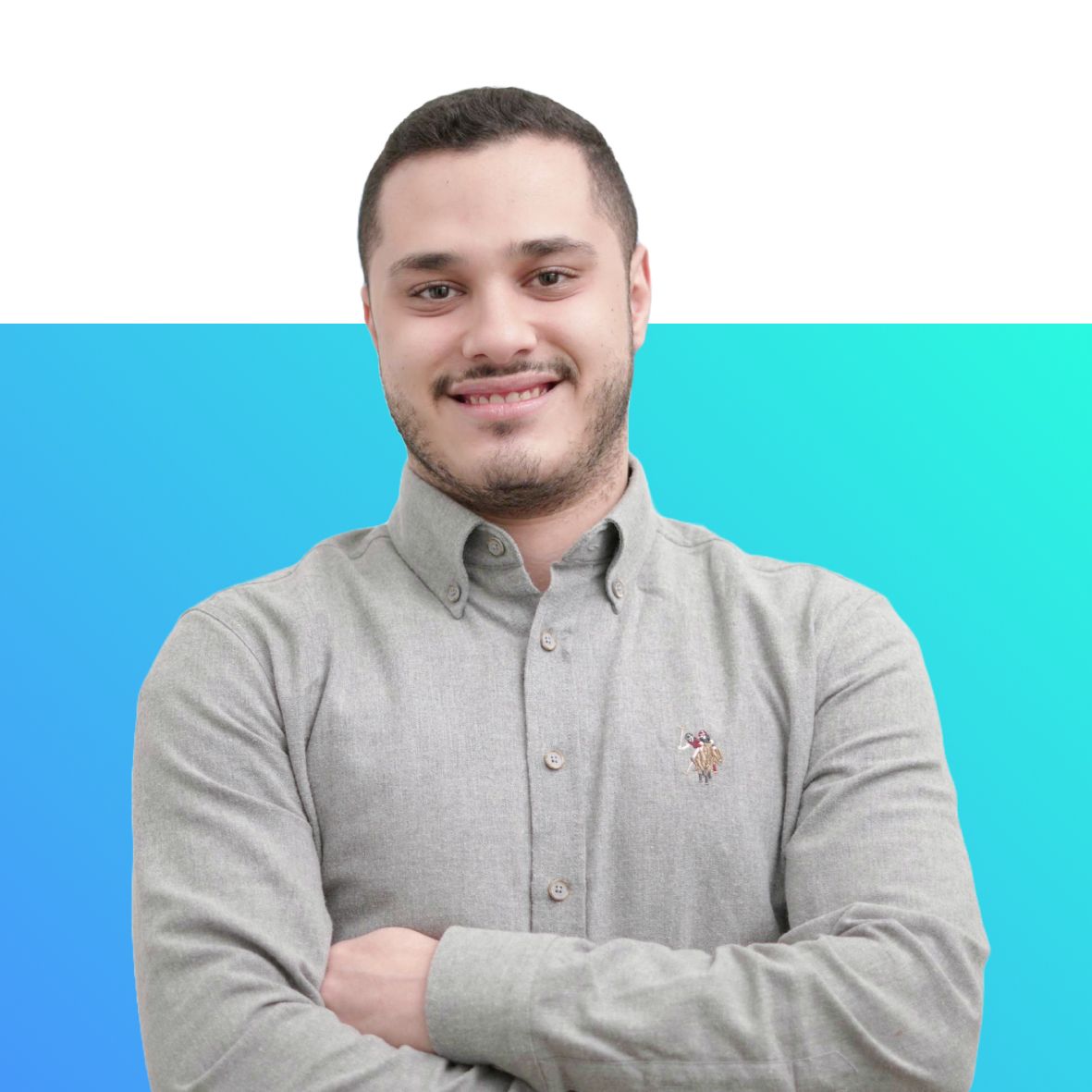 A man in a grey shirt is smiling with his arms crossed