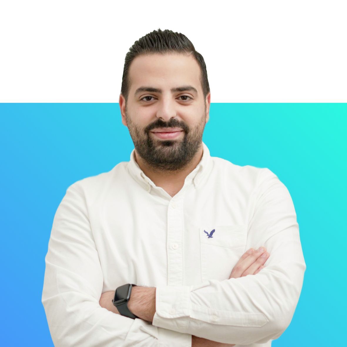 A man with a beard wearing a white shirt has his arms crossed