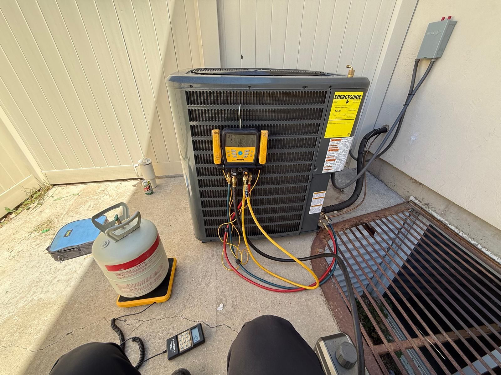HVAC technician working on an AC unit outdoors. Gauges and gas tank present.