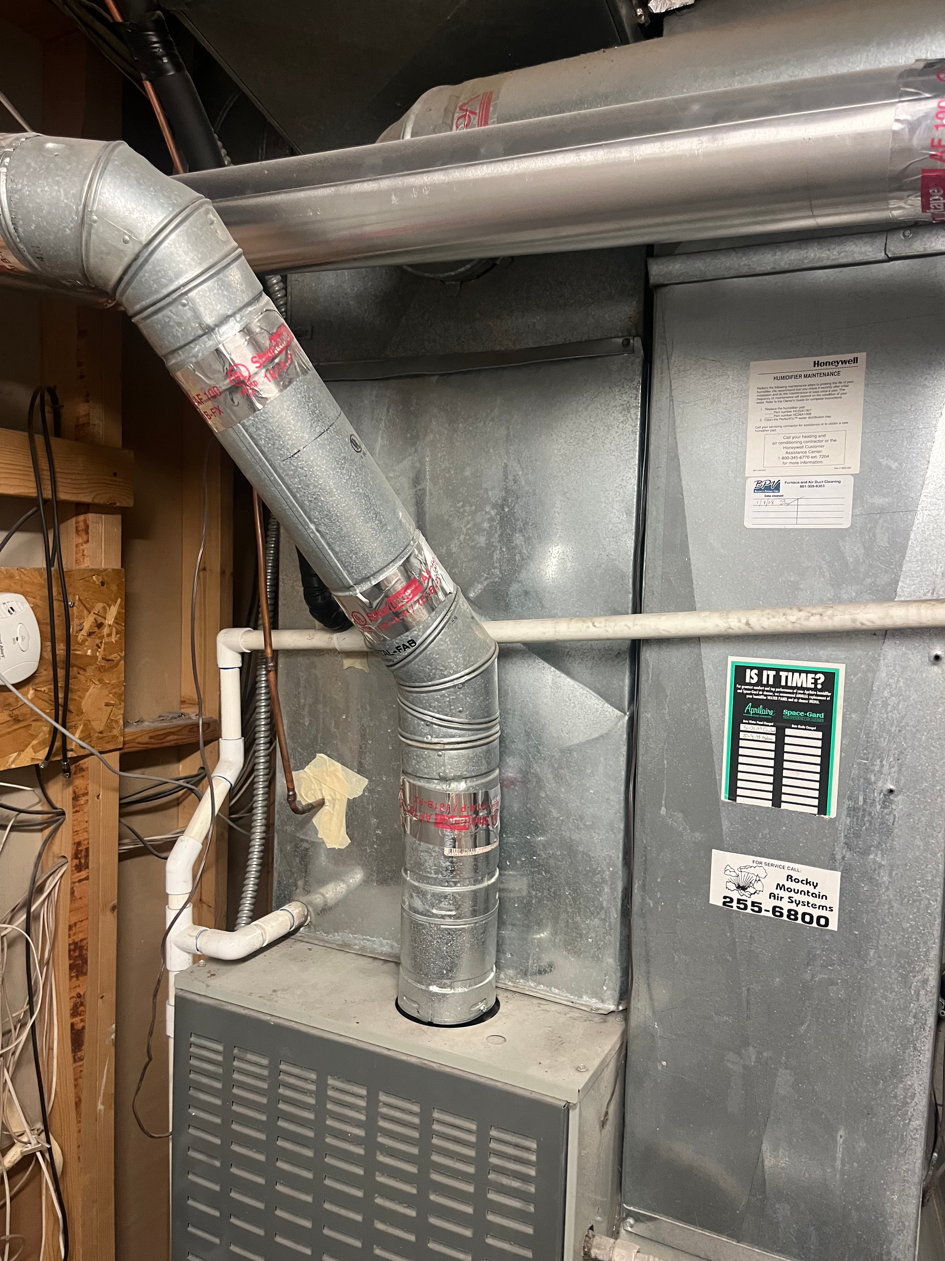 Furnace with metallic ductwork, pipes, and electrical wiring in a utility room.