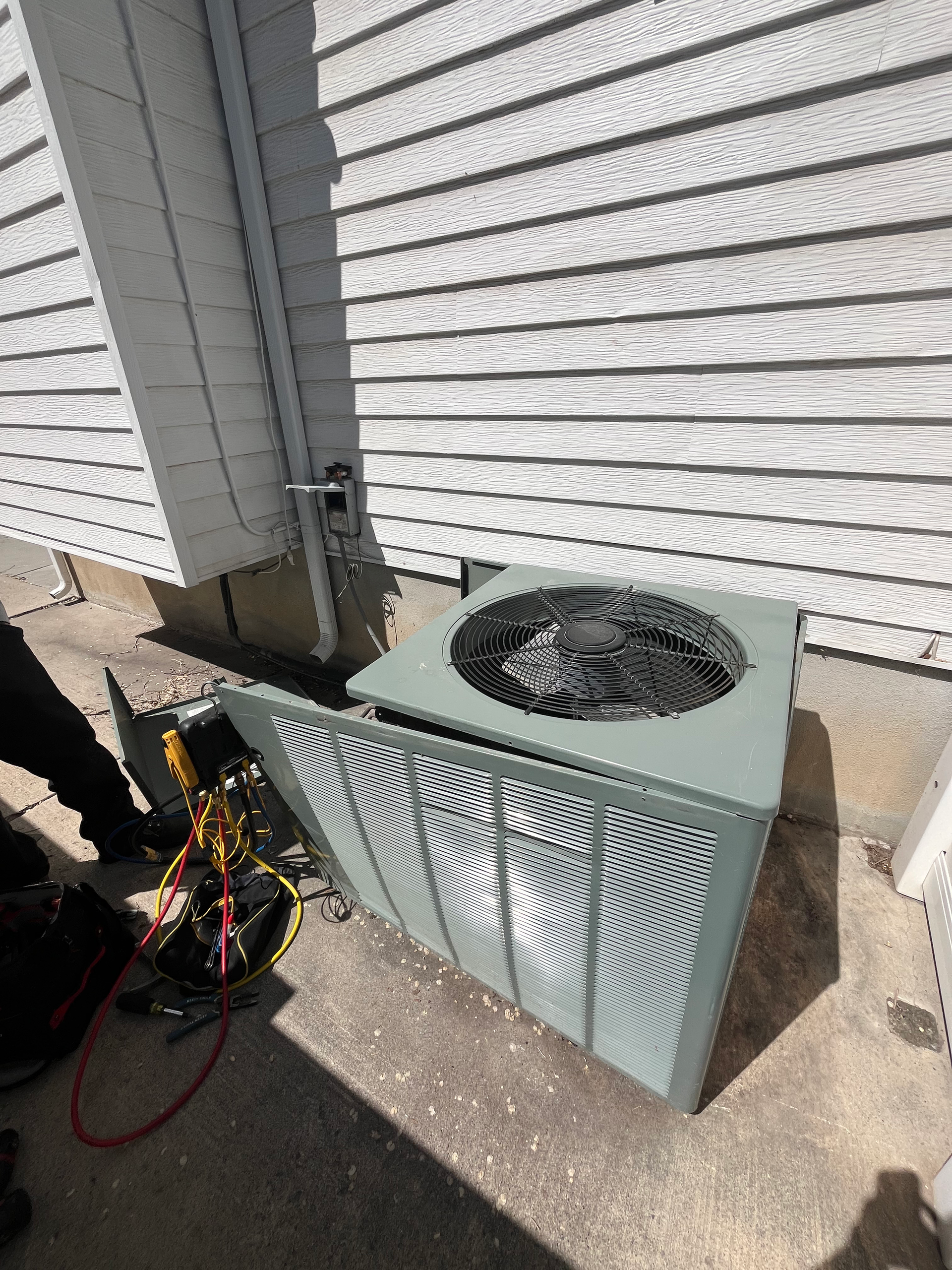 HVAC unit outdoors, panel open. A person working on the unit near a siding wall.