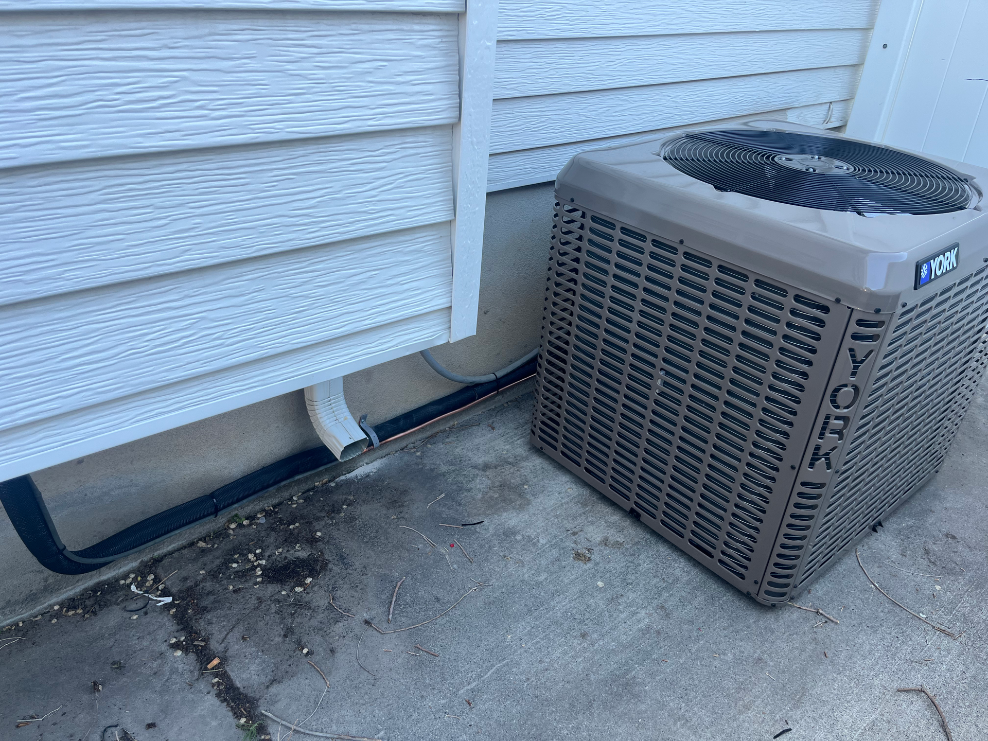 A York air conditioning unit sits next to a house with white siding and gray concrete.