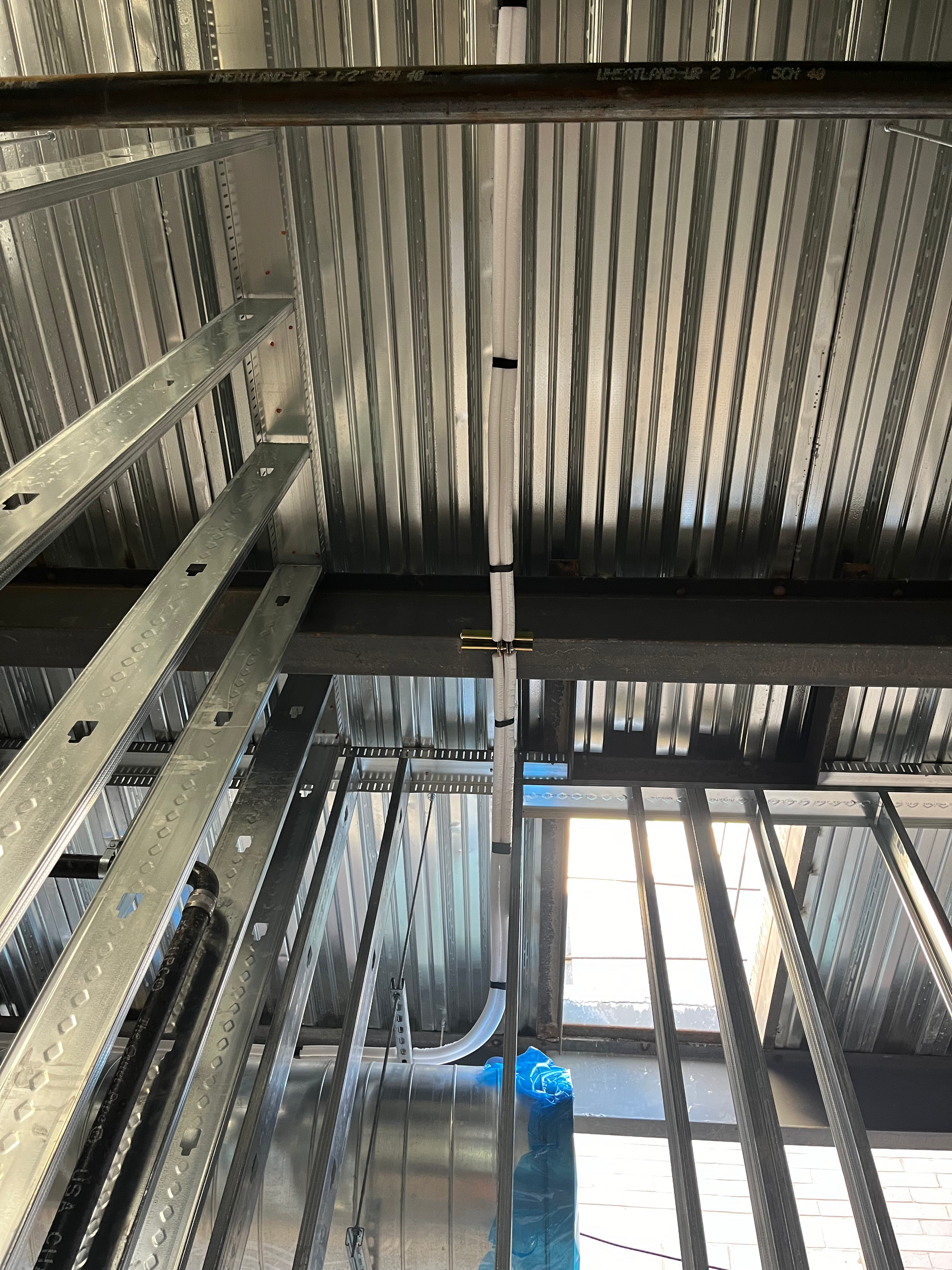 Construction site interior: Metal beams, corrugated decking, wiring conduit suspended from the ceiling.