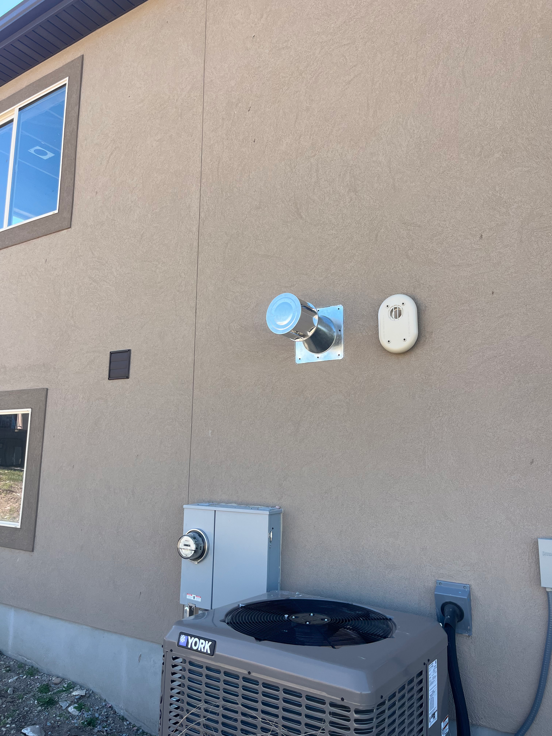 Exterior of a stucco house with an AC unit, electrical box, and vents mounted on the wall.