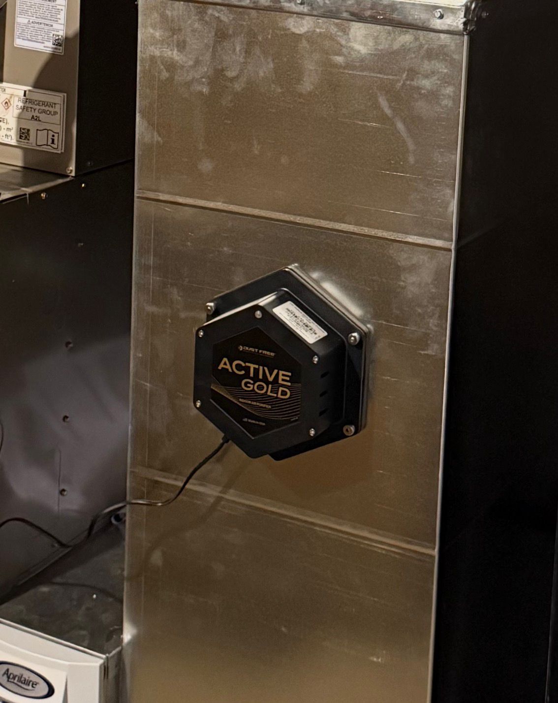 Active Gold air purifier installed on a silver HVAC duct in a dark room.