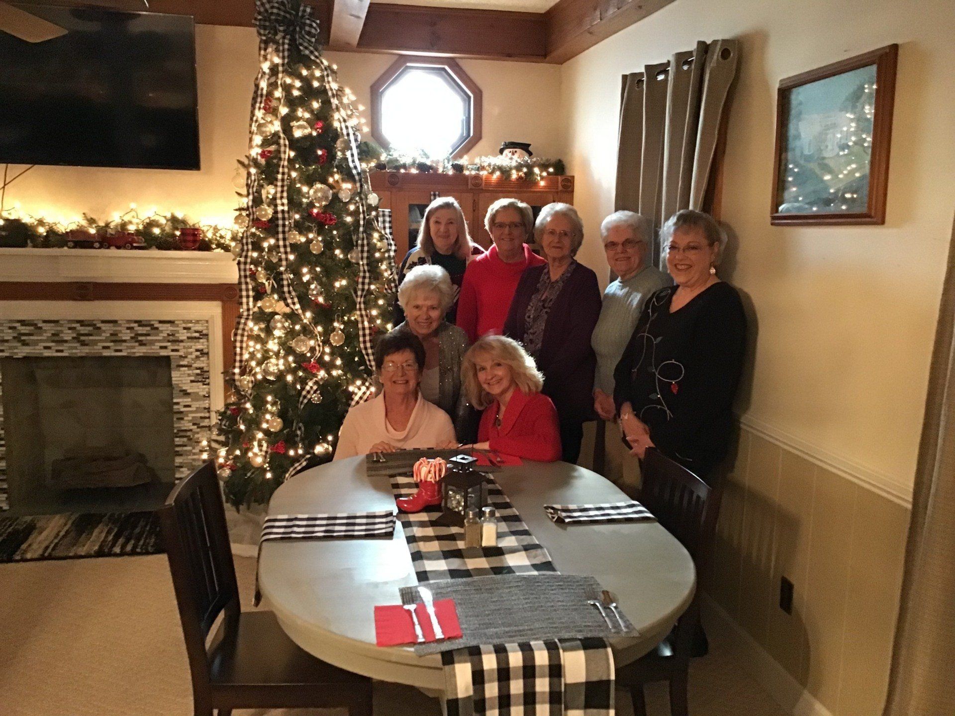 A group of women are sitting at a table in front of a christmas tree.
