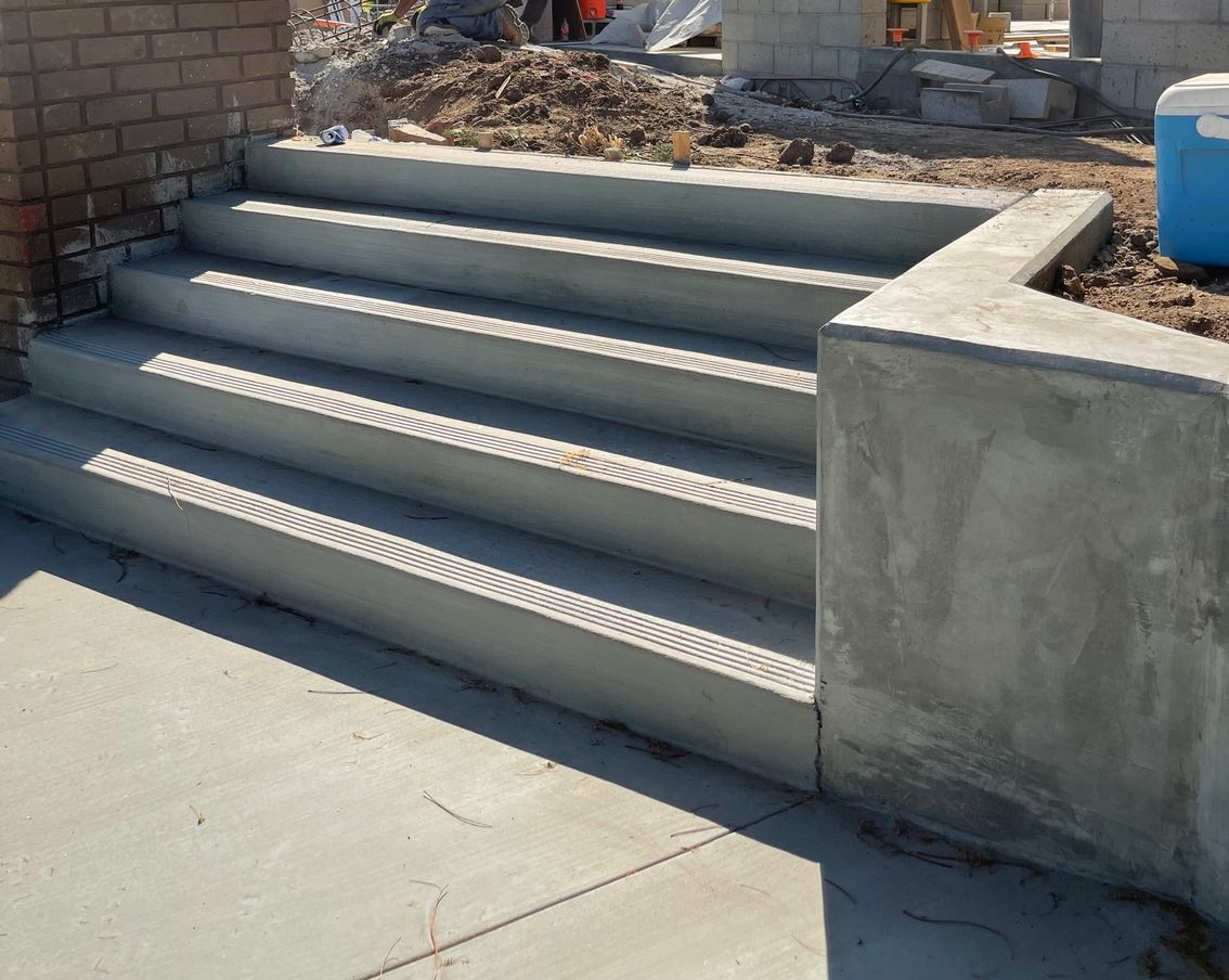 Concrete steps with metal anti-slip treads leading up to a raised landing outdoors under construction.
