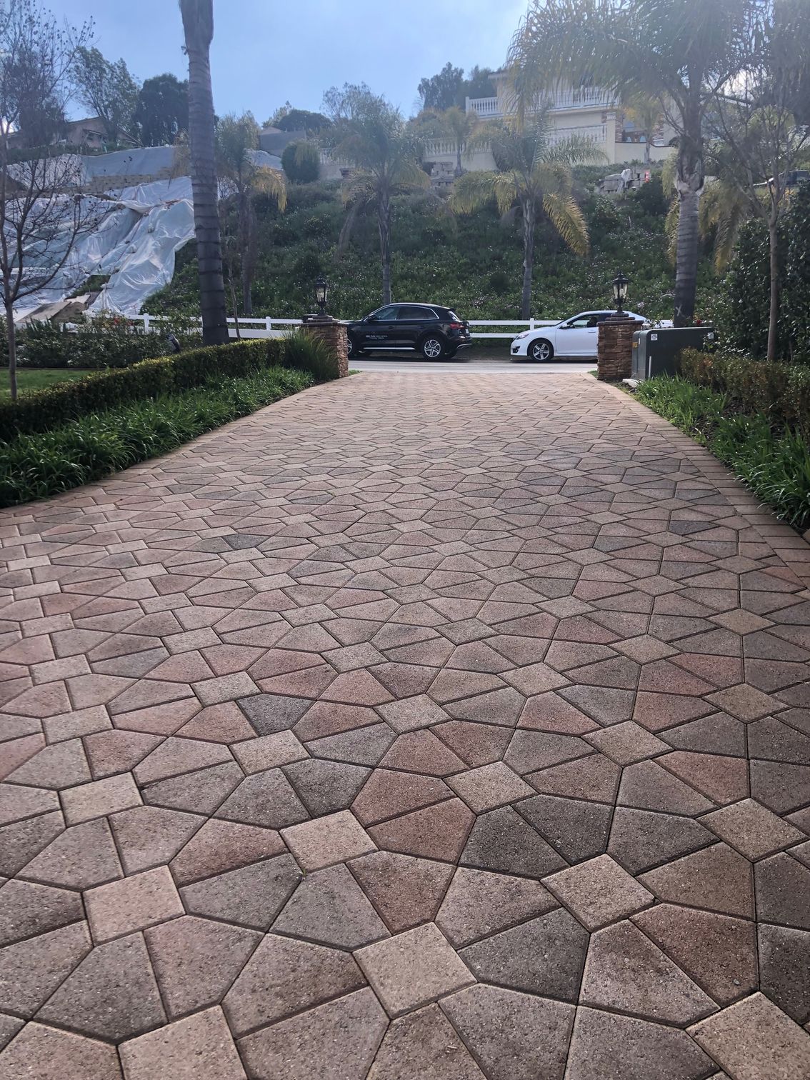 Stone-paved driveway leading to parked cars, with landscaped hills and trees in the background