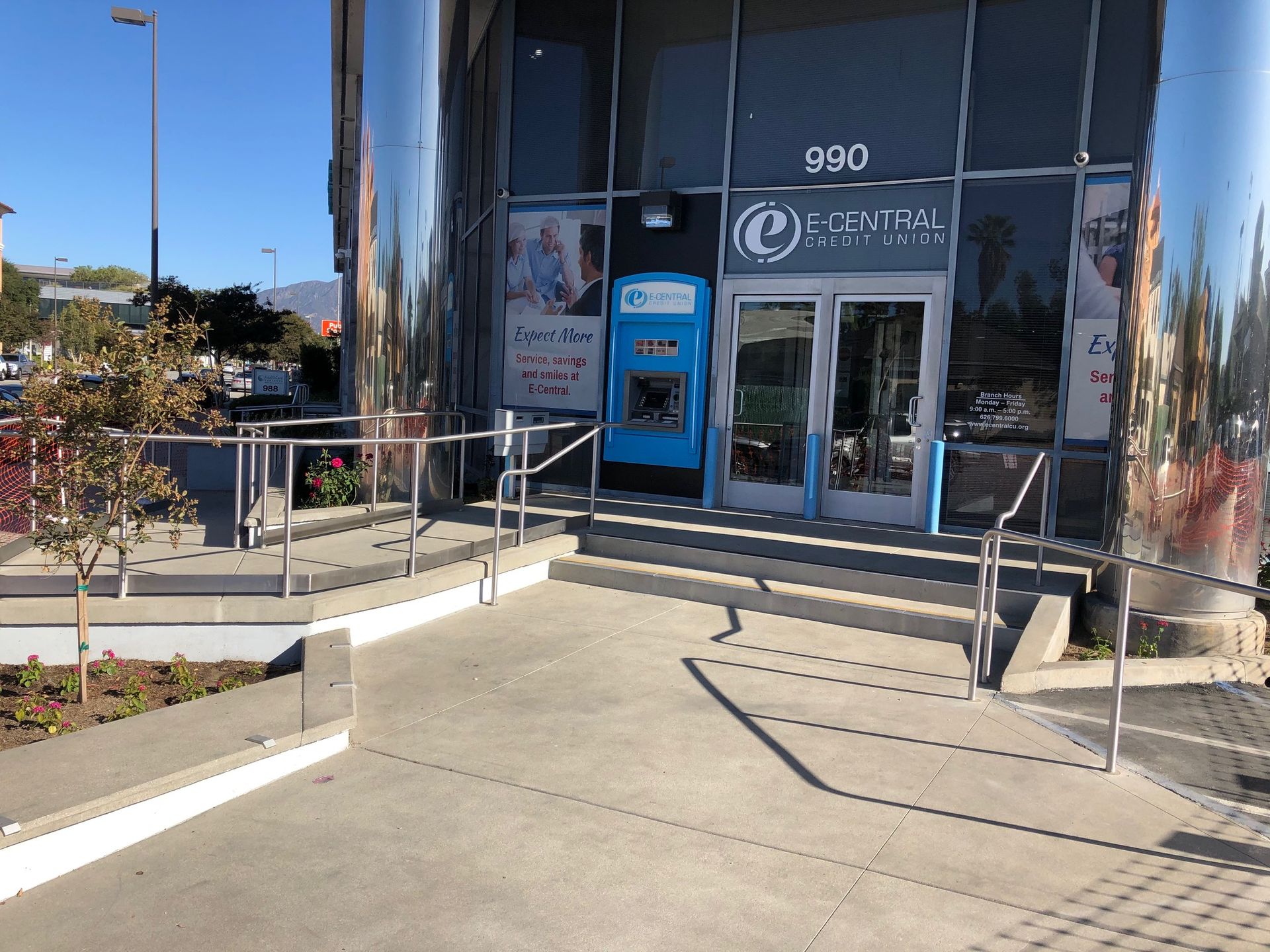 Storefront entrance with glass doors, blue ATM kiosk, and wheelchair ramp leading up to the building.