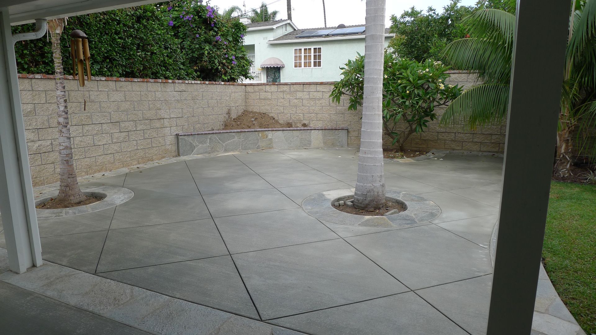 Patio with concrete pavers, two palm trees, and a stone wall in the background