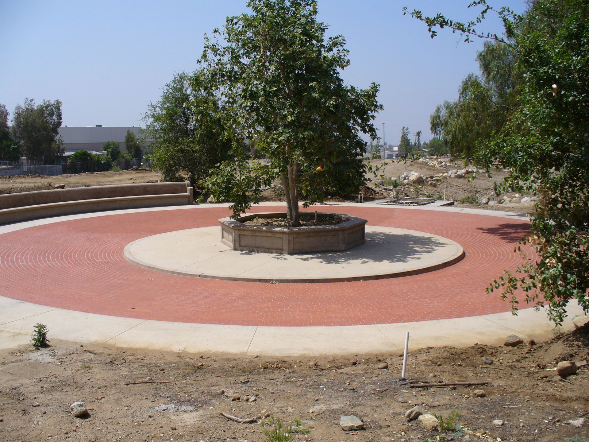 Circular red walkway around a central planter with trees in a dry landscaped park.