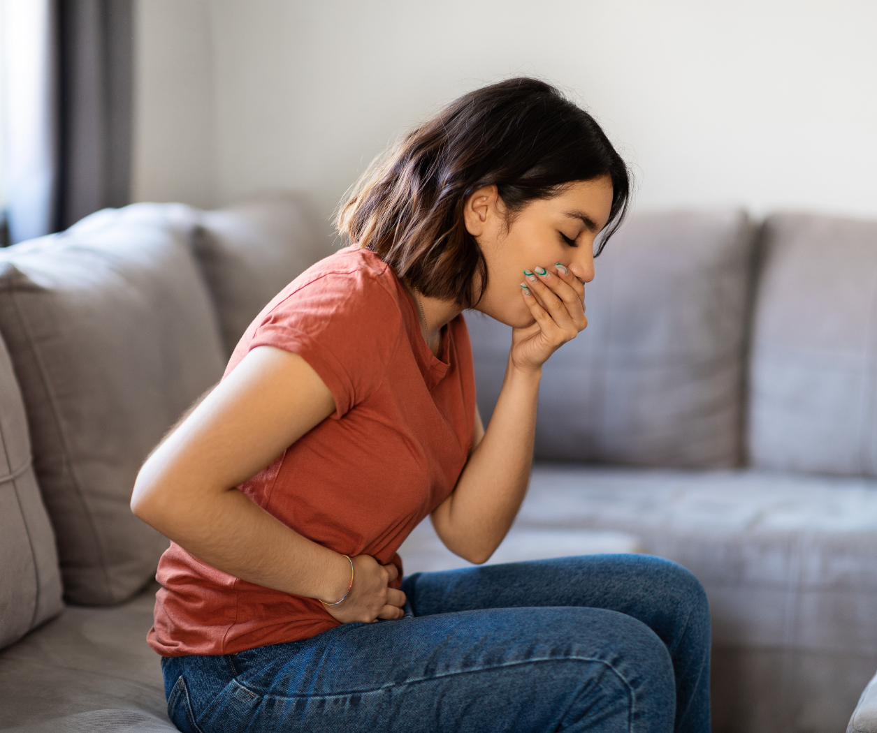 A woman is sitting on a couch with her hands on her stomach.
