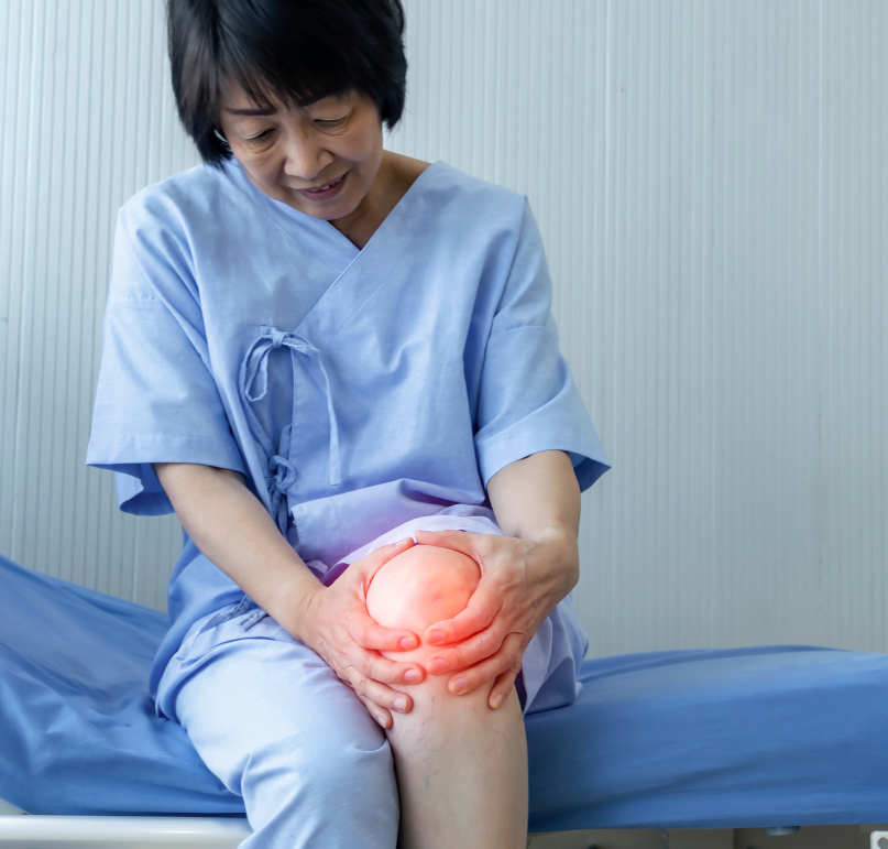 Woman seated on a bed, holding her painful knee. Red highlight indicates pain.