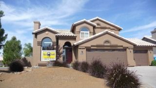 Suburban stucco house with a yellow real estate sign in front, desert landscaping, and a blue sky