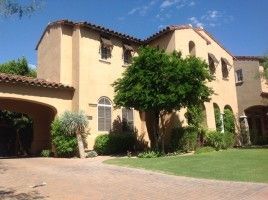 Stucco Mediterranean-style house with red-tiled roof, arched entry, and green lawn under a blue sky