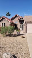 Desert-style house with tan stucco, red roof, gravel yard, cactus shrubs, and a palm tree under a clear blue sky