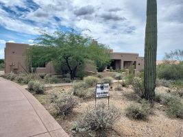 Desert home with cactus, shrubs, and a sidewalk in the foreground under a cloudy sky