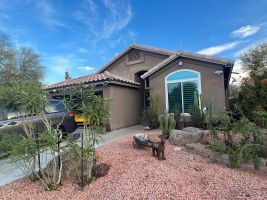 Front view of a tan stucco house with a tiled roof, arched window, and desert landscaping.