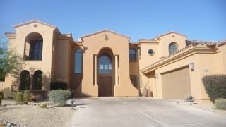 Large tan stucco house with arched windows, double garage, and a driveway in front.