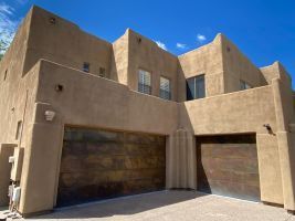 Sunlit adobe-style building with tan stucco walls, wooden garage doors, and blue sky above