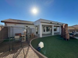 Backyard patio with artificial grass, white pergola, and outdoor furniture under a bright sun