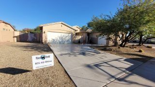 Desert suburban house with a long concrete driveway and a real estate sign in front