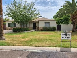 Single-story house with palm trees and a lawn, with a real estate sign by the curb.