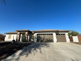 Single-story stucco house with a large garage, driveway, and clear blue sky.