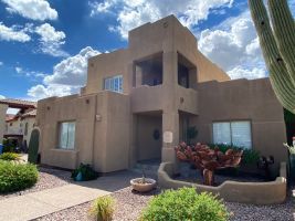 Tan stucco two-story house with desert landscaping under a bright blue sky