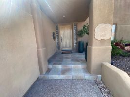 Covered front walkway with stucco walls, tiled path, and a front door at the end.