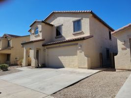 Suburban stucco house with a two-car garage and driveway under a clear blue sky