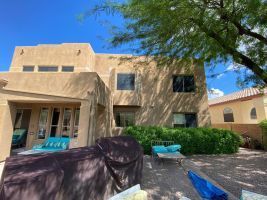 Desert-style stucco house with patio chairs, shrubs, and a blue sky.