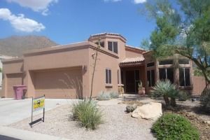 Single-story desert-style house with tan stucco, a garage, and xeriscaped front yard under a blue sky