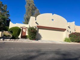 Cream stucco house with a two-car garage, red trim, and desert landscaping on a sunny street.