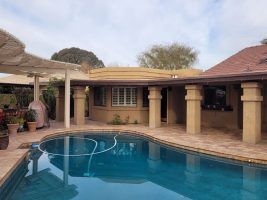 Backyard patio with a blue swimming pool beside a beige house and covered seating area