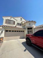 Two-story beige house with a two-car garage and a red SUV parked in the driveway under a clear blue sky